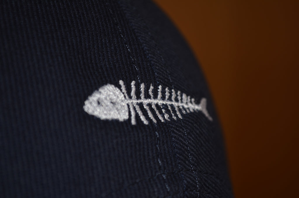 dettaglio del ricamo con lisca di missoltino o missultino sul dietro di cappellino baseball o da camionista blu con logo misultin zone ricamato in bianco sul fronte e sul retro
